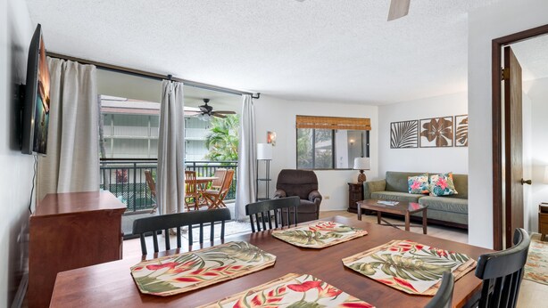 A modern living room with a dining area, a sofa, a TV, and a balcony with a view. - Big Island Kona Ali'i by Coldwell Banker Island Vacations (Kailua-Kona)
