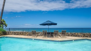 A poolside area with lounge chairs and an umbrella, overlooking a clear blue ocean.