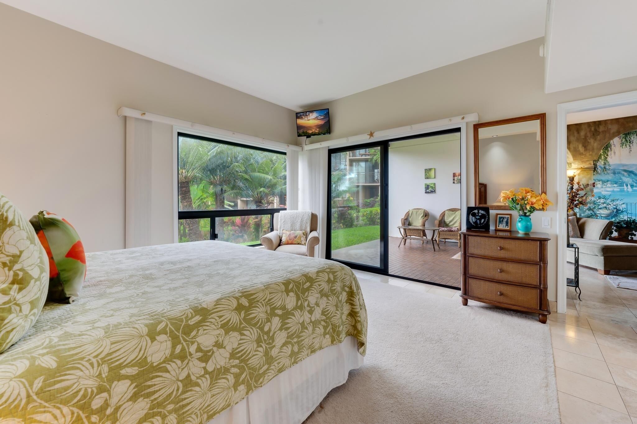 Ein Schlafzimmer mit Bett, Kommode, Fernseher und einer Schiebetür zu einem Balkon.