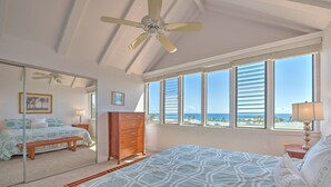 A bedroom with a bed, a dresser, a mirror, and a view of the ocean through large windows. - Kauai Makanui by Coldwell Banker Island Vacations (Koloa)