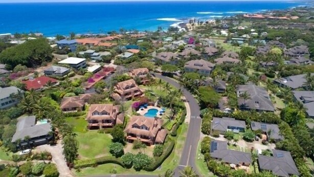 An aerial view of a residential area with houses, a winding road, and a large body of water in the background. - Kauai Makanui by Coldwell Banker Island Vacations (Koloa)
