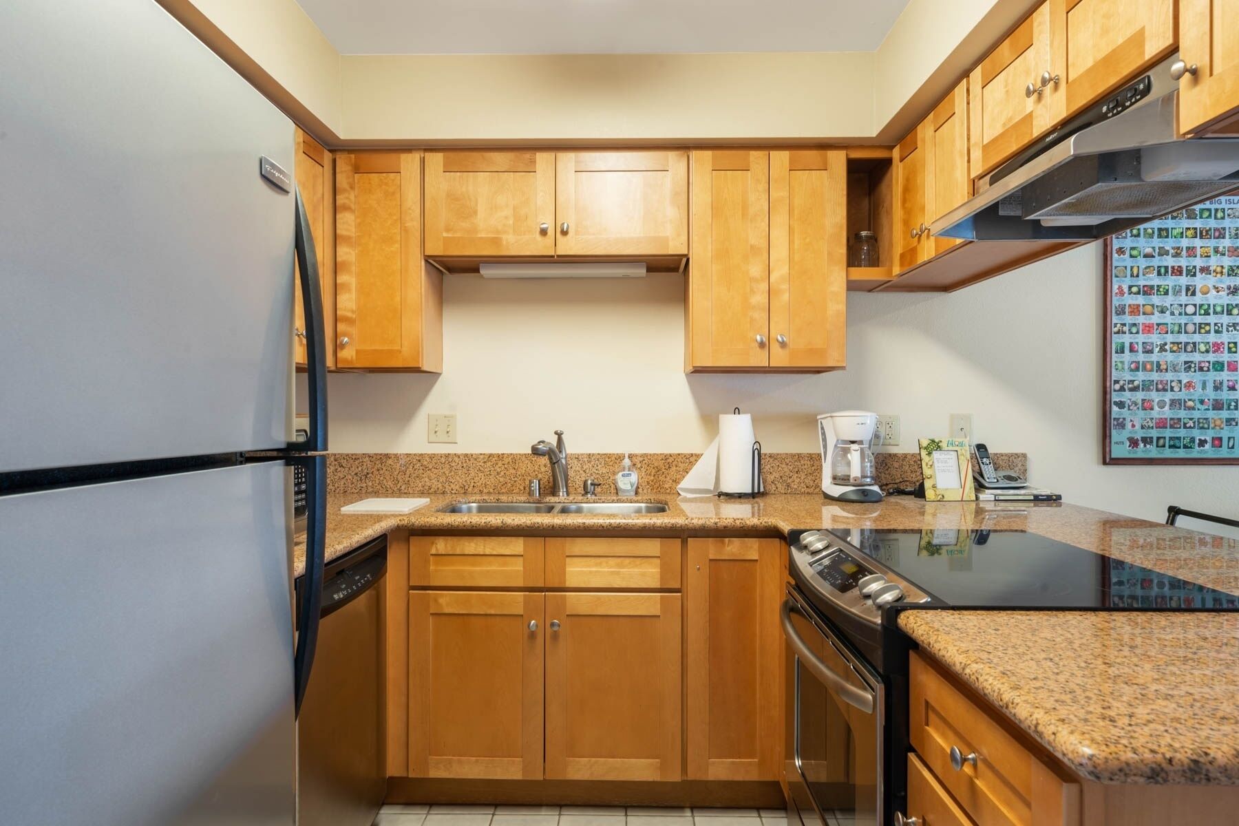 A compact kitchen with wooden cabinets, a stainless steel refrigerator, a built-in oven, and a granite countertop.