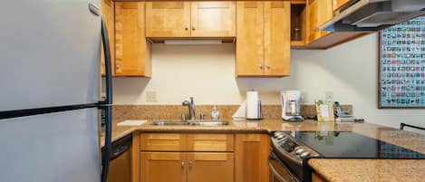 Una cocina compacta con armarios de madera, un refrigerador de acero inoxidable, horno integrado y encimera de granito.