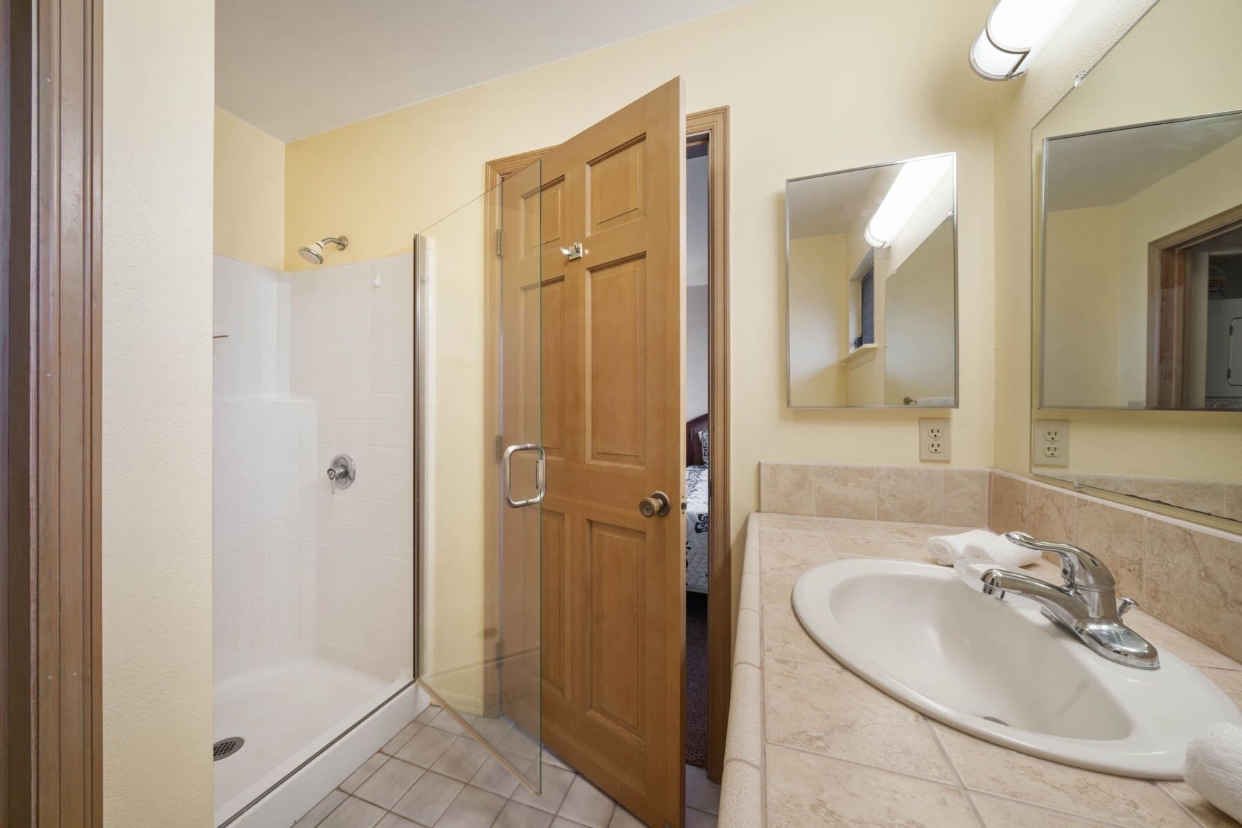 A bathroom with a shower, a sink, a mirror, and a wooden door.