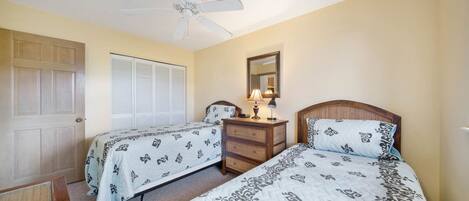 A bedroom with two beds, a ceiling fan, a bedside table with a lamp, and a mirror on the wall.