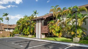 A parking lot with marked spaces, a building with a balcony, and palm trees.