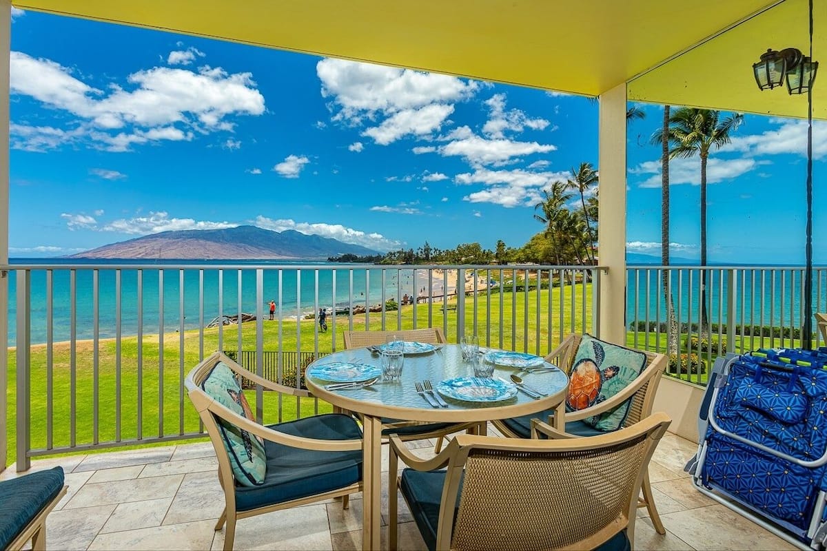 Un balcon avec une table dressée pour le dîner, offrant une vue sur une plage et une montagne.