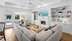 A spacious living room with a large sofa, a fireplace, and a television mounted on the wall. - Sweet Spot - Newly Renovated, Heated Pool, Golf Cart, Deeded Beach Access! (Miramar Beach)