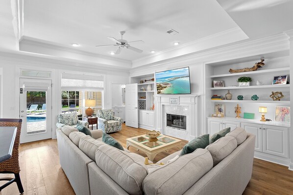 A spacious living room with a large sofa, a fireplace, and a television mounted on the wall.