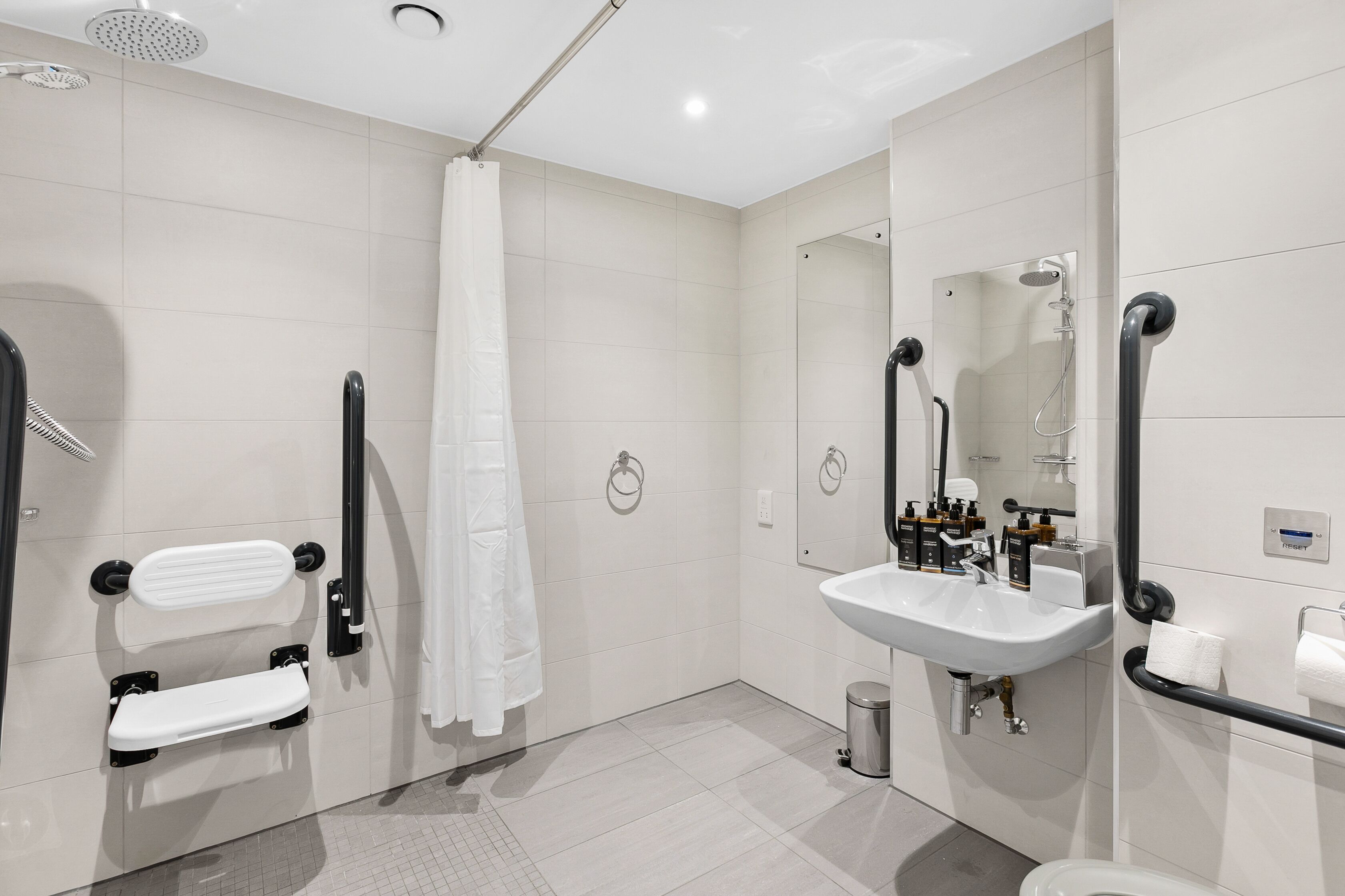 A modern bathroom with a white sink, a mirror, a shower, and a toilet.
