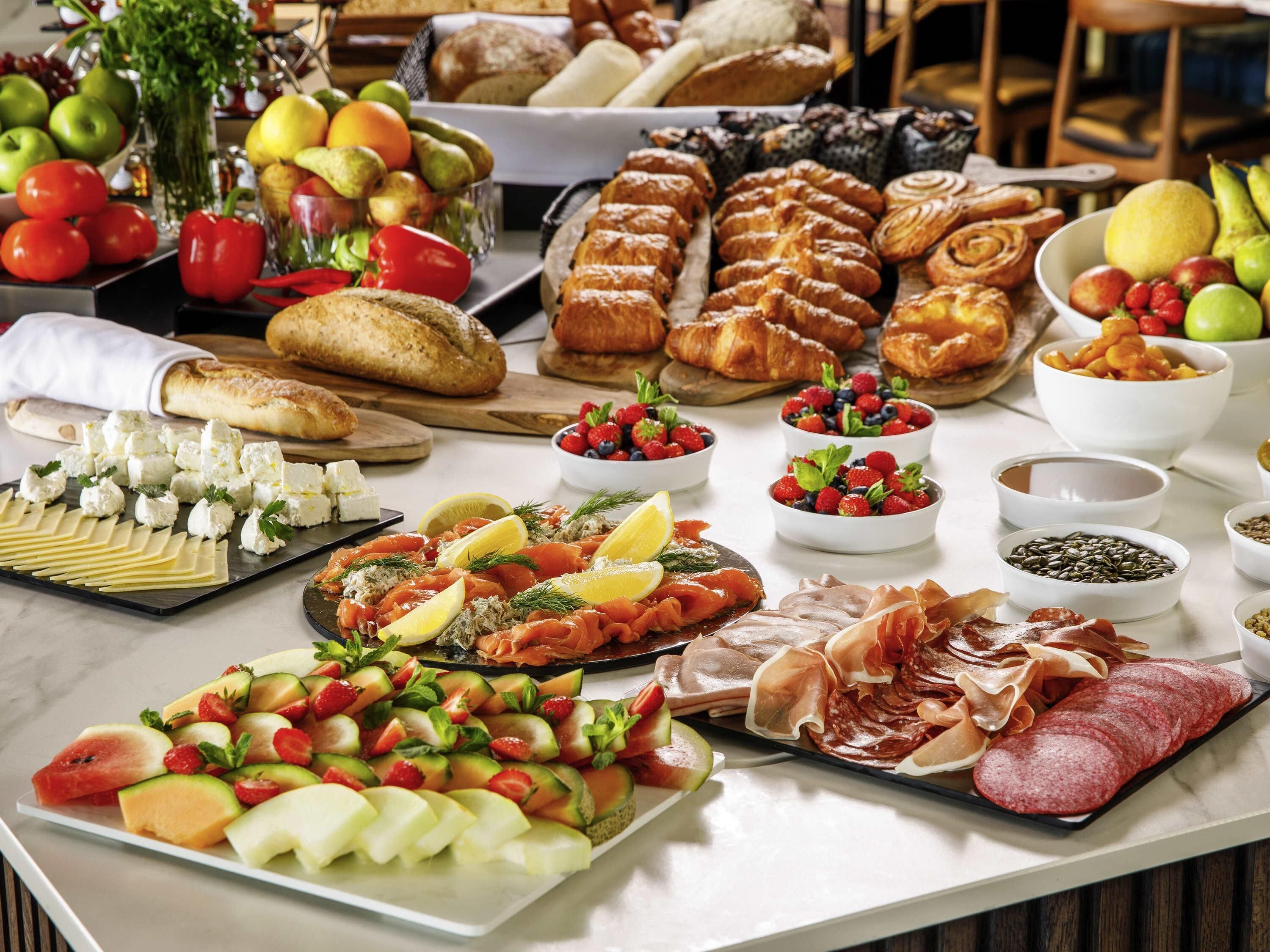 Una mesa de buffet con diversos alimentos, incluyendo frutas, quesos, pasteles y carnes.