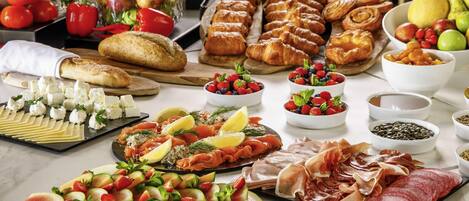 A buffet table with various food items including fruits, cheeses, pastries, and meats.
