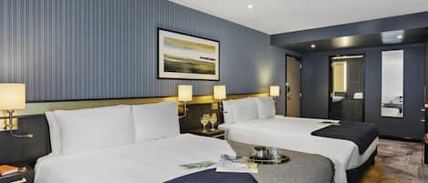 A hotel room with two beds, a large framed picture on the wall, and a bathroom visible through an open door.