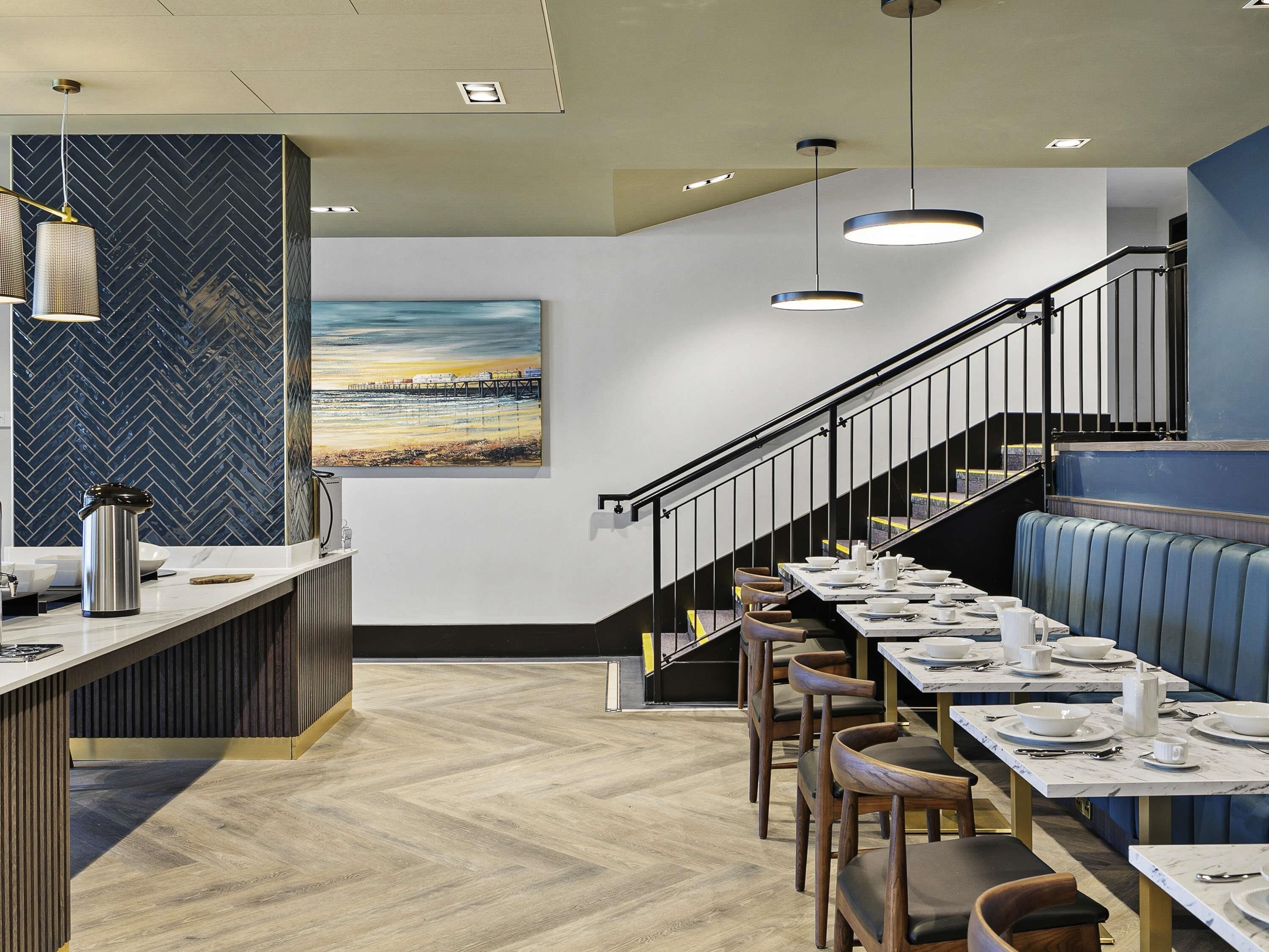 A restaurant with a herringbone floor, a counter with a kettle, and a staircase with a railing.