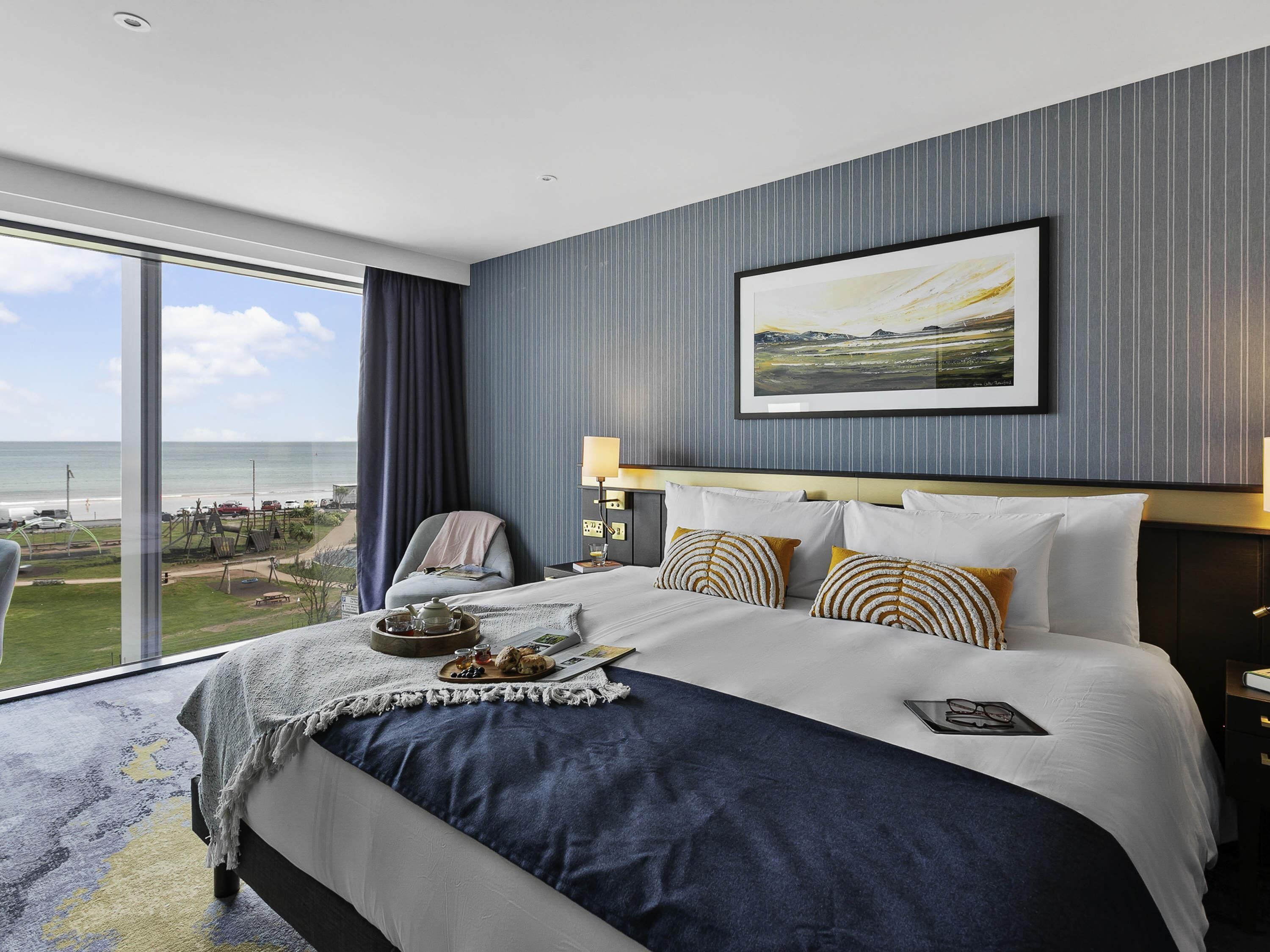 Un cuarto de hotel con una cama grande, vista a la playa y un cuadro en la pared.