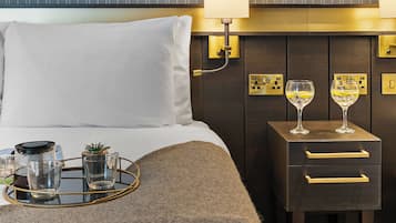 Habitación de hotel con cama, lámparas de noche, una mesita de noche con dos copas de vino y una bandeja con copas y una botella.