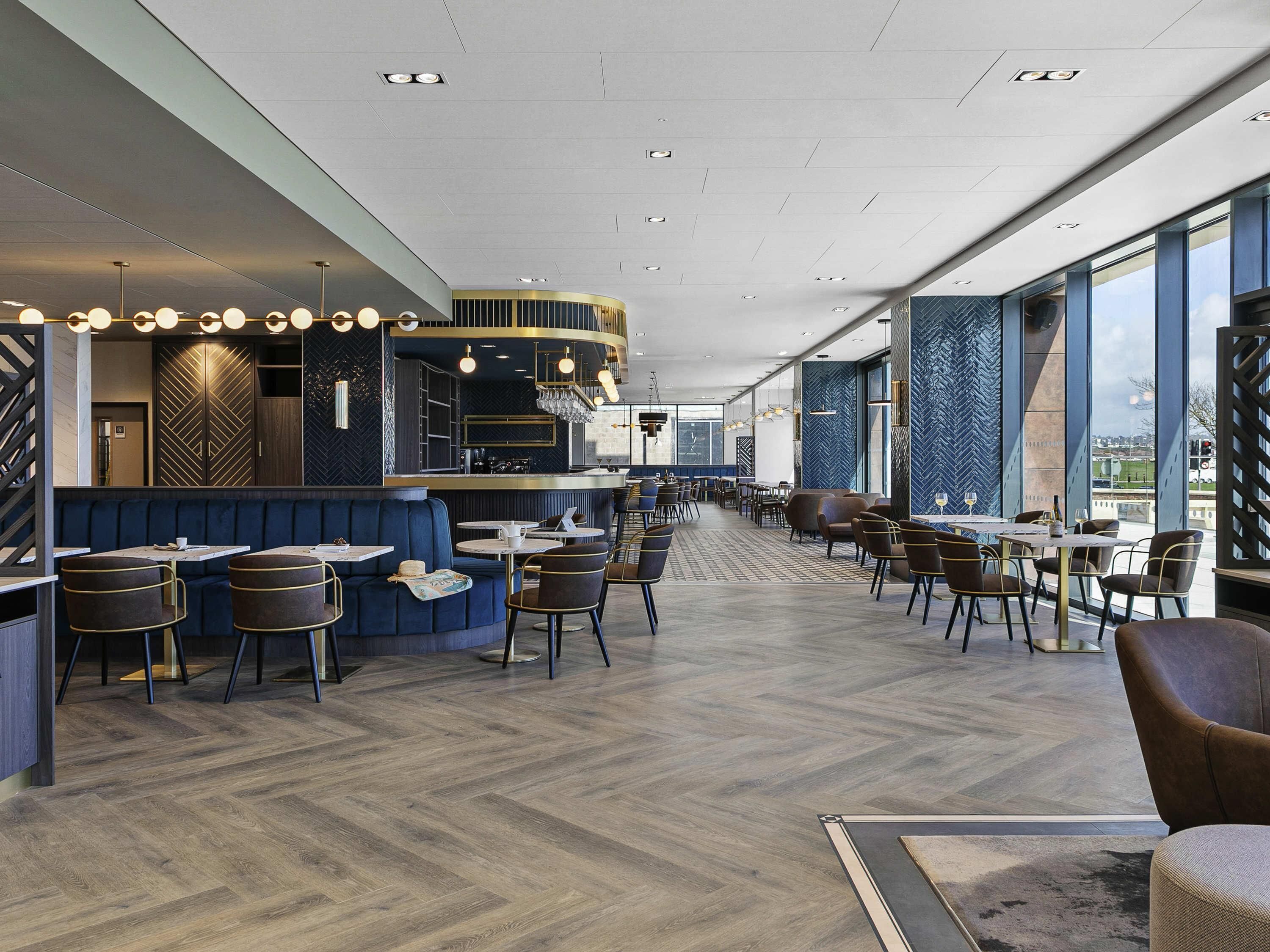 Ein modernes Restaurantambiente mit Bar, Sitzgelegenheiten und großen Fenstern.