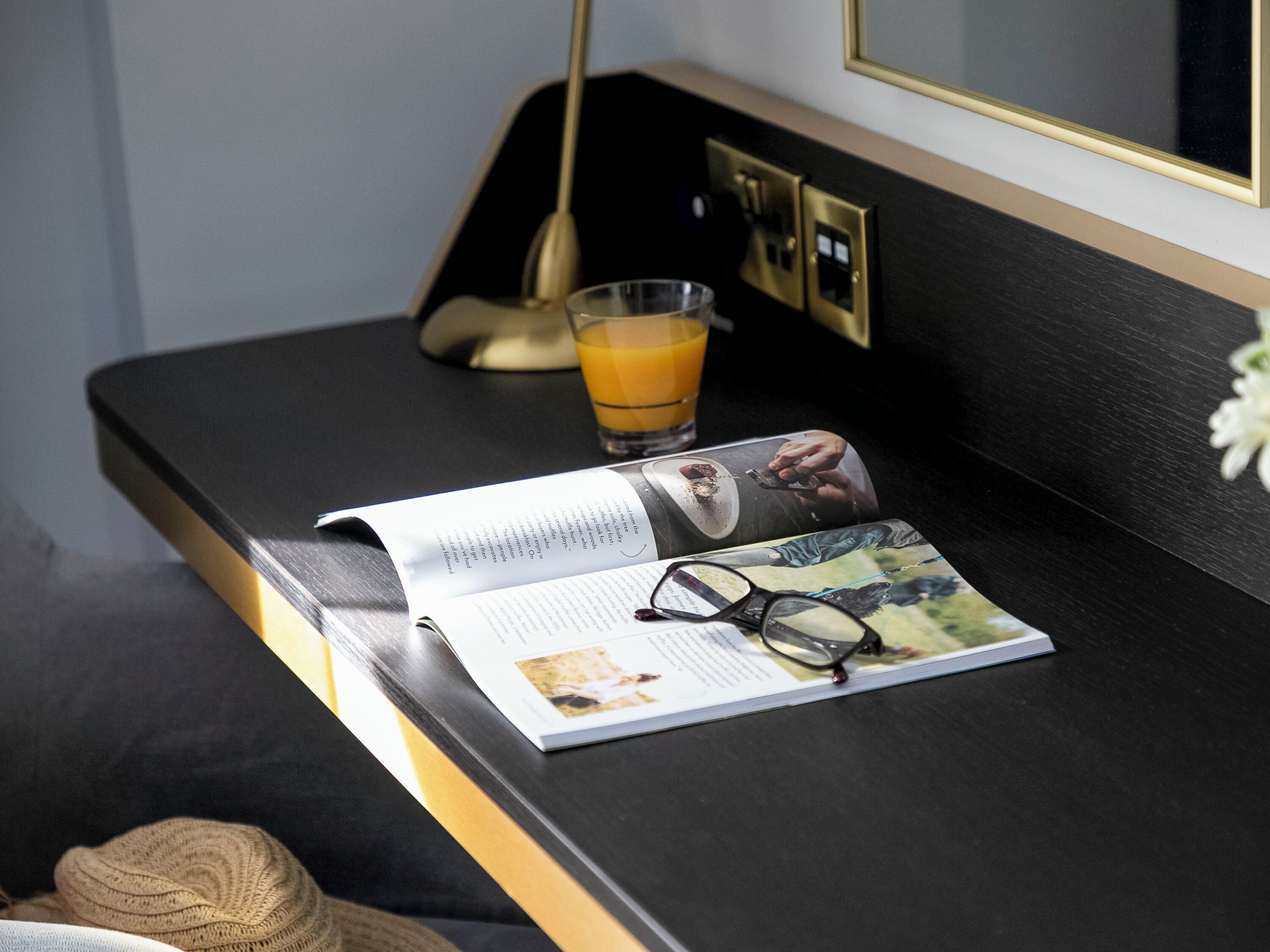 A magazine on a black table with a glass of orange juice, a pair of glasses, and a remote control.