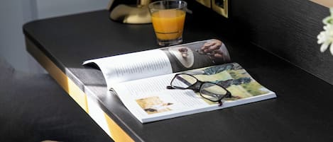 A magazine on a black table with a glass of orange juice, a pair of glasses, and a remote control.