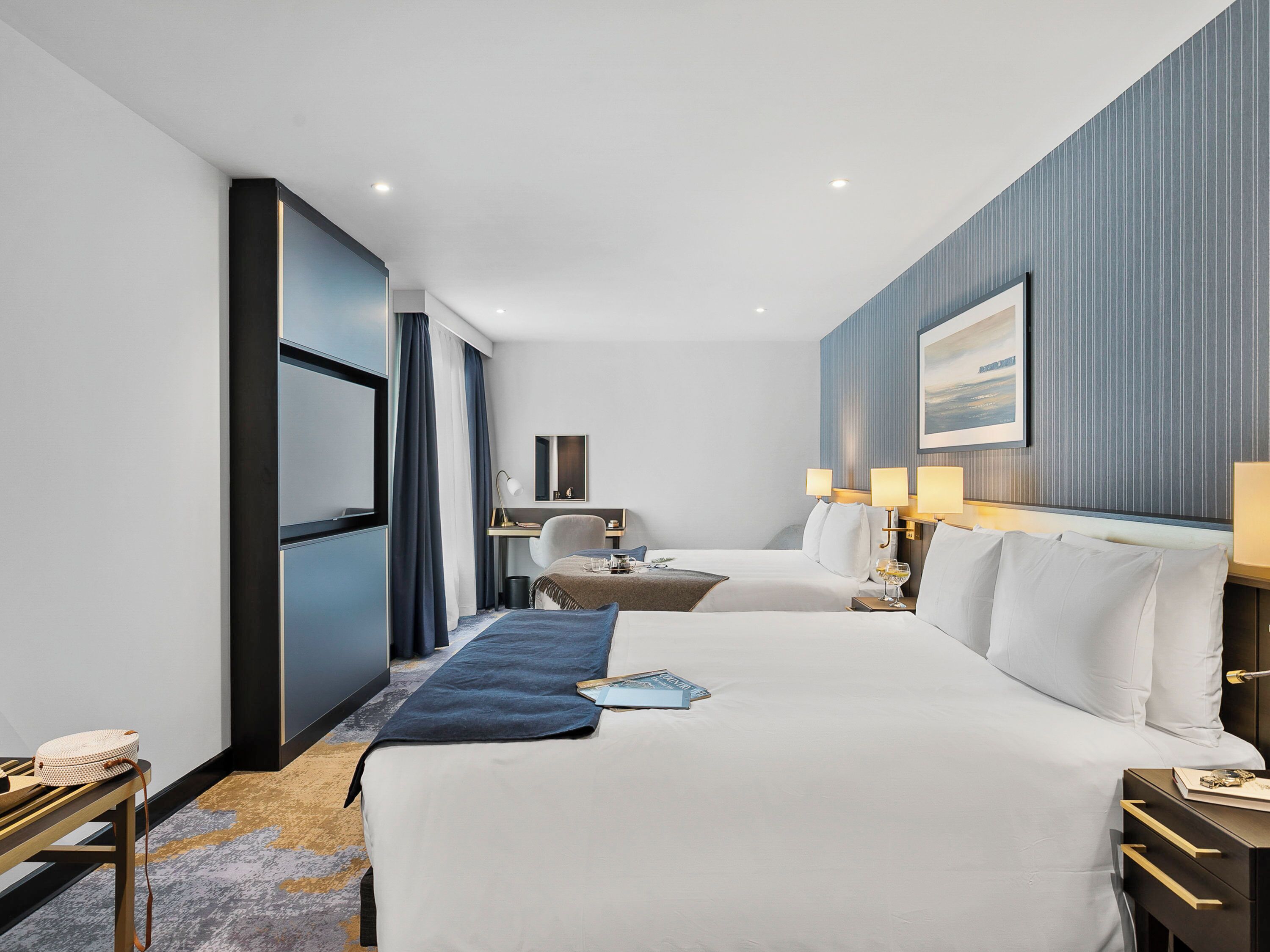 A hotel room with two beds, a desk, a chair, and a large window.