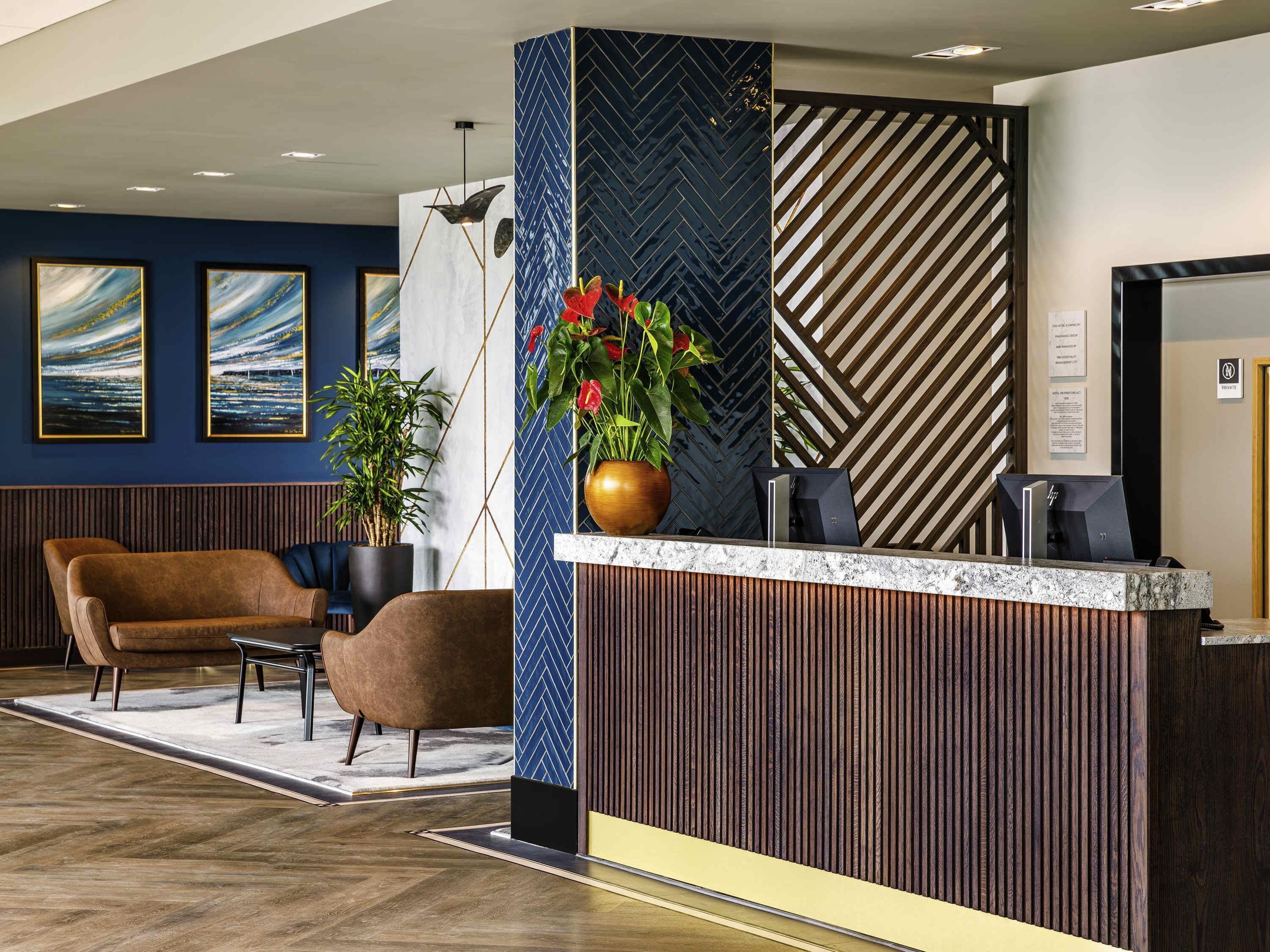 A reception area with a wooden reception desk, a brown leather sofa, and two framed artworks on the wall.