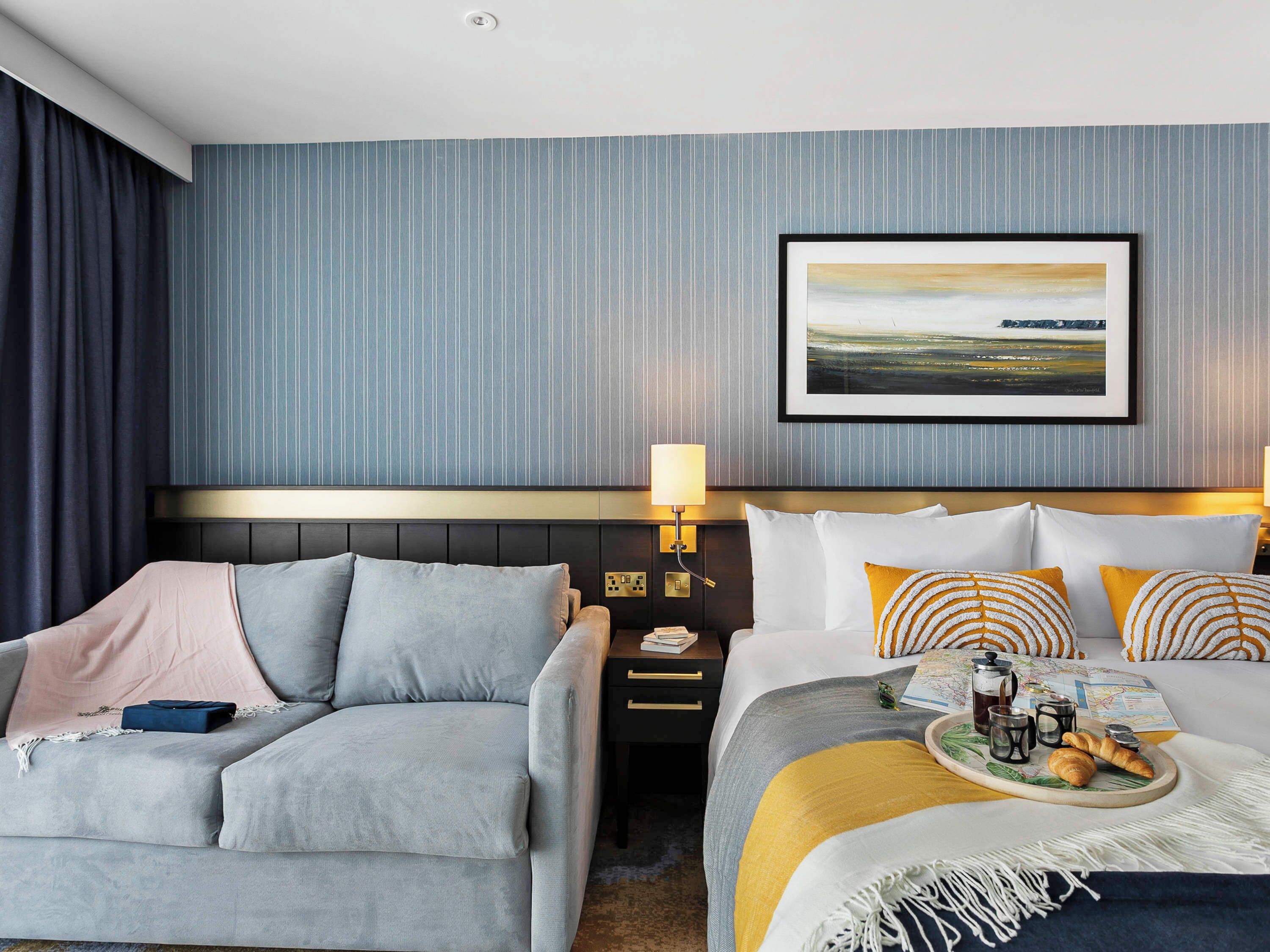 Ein Hotelzimmer mit einem Bett, einem Schlafsofa, einem Nachttisch, einer Lampe und einem gerahmten Bild an der Wand.