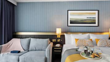 A hotel room with a bed, a sofa, a nightstand, a lamp, and a framed picture on the wall.