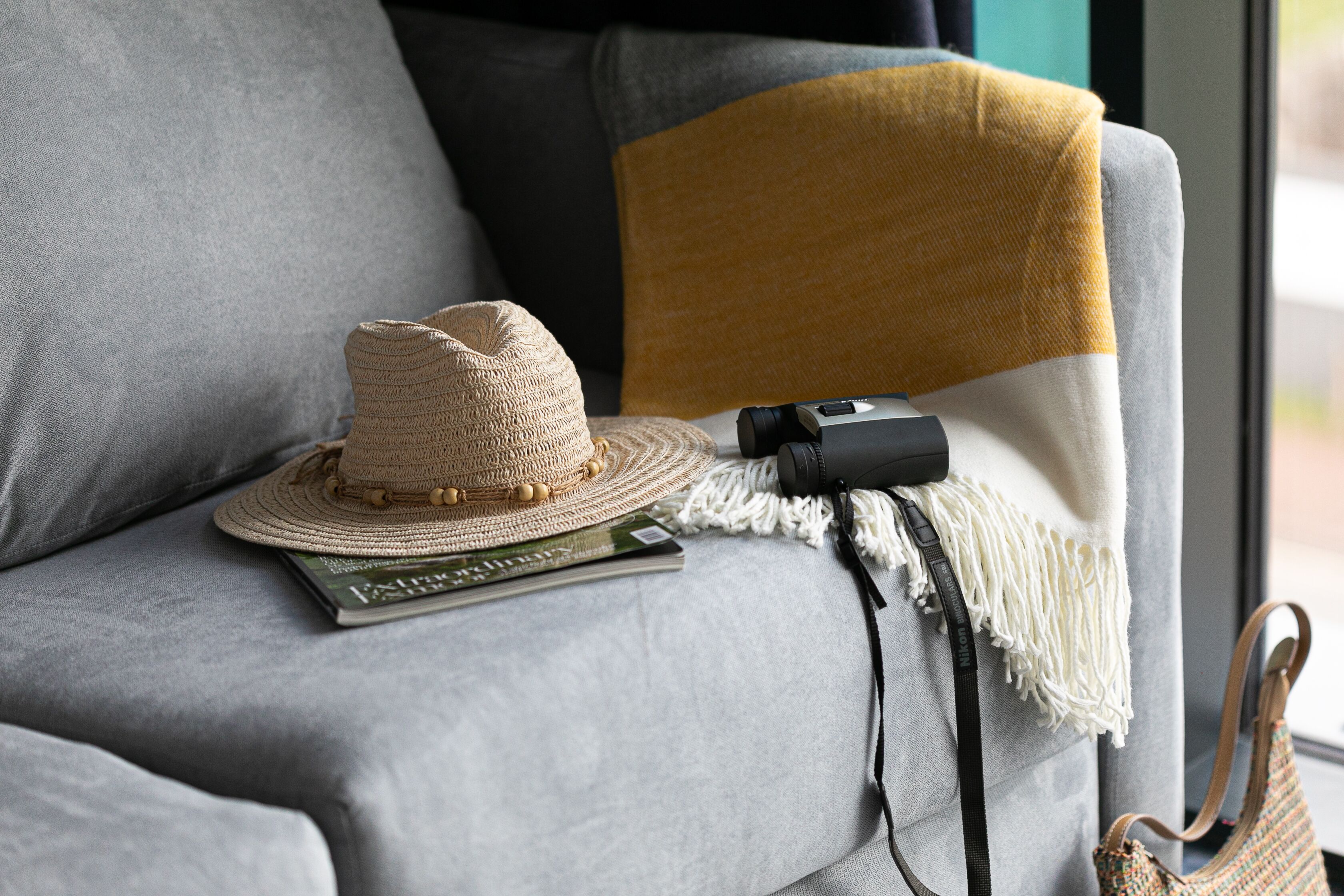 A grey sofa with a woven hat, a camera, and a magazine on it.