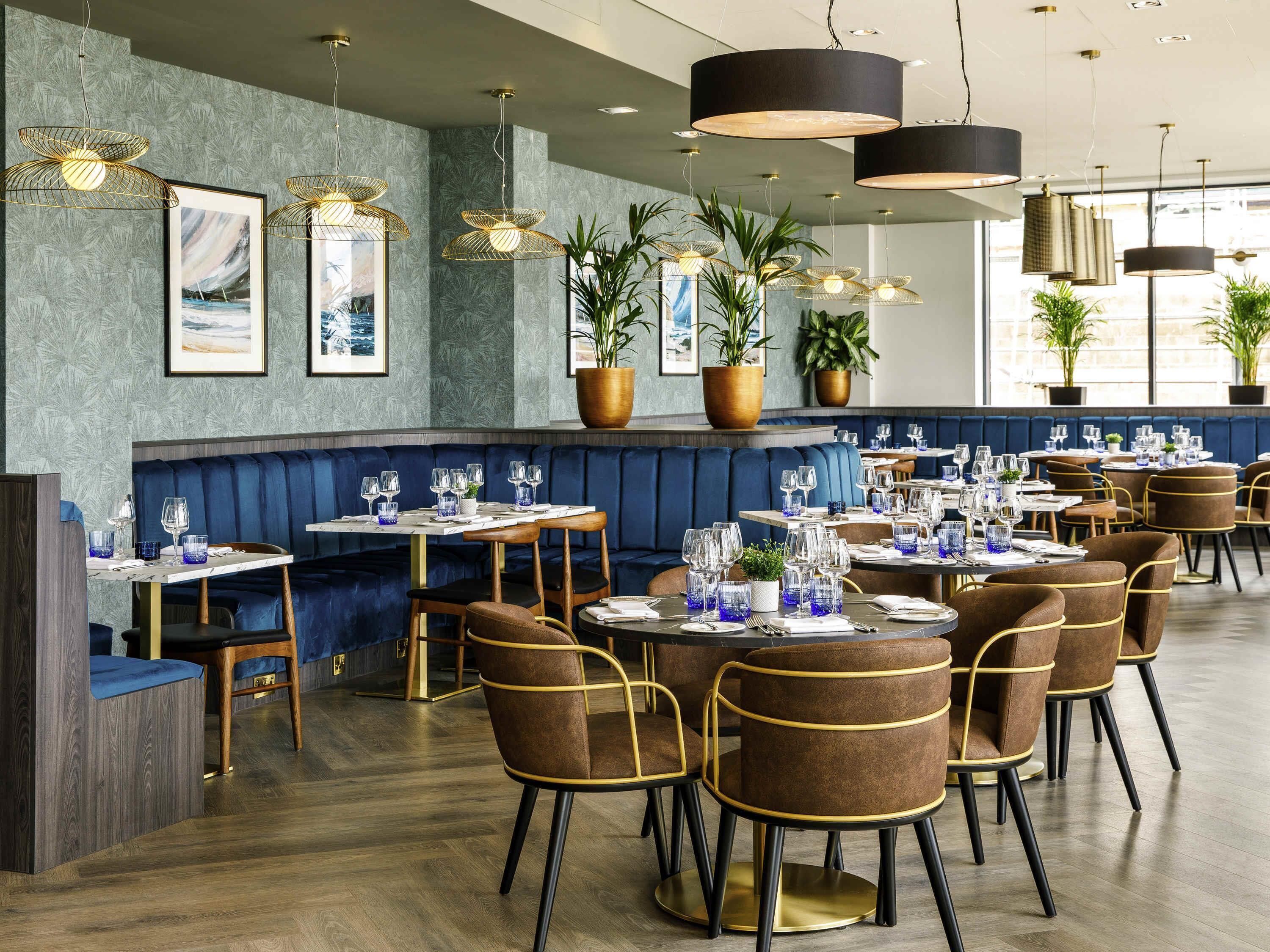 A restaurant interior with booths, round tables, and hanging pendant lights.