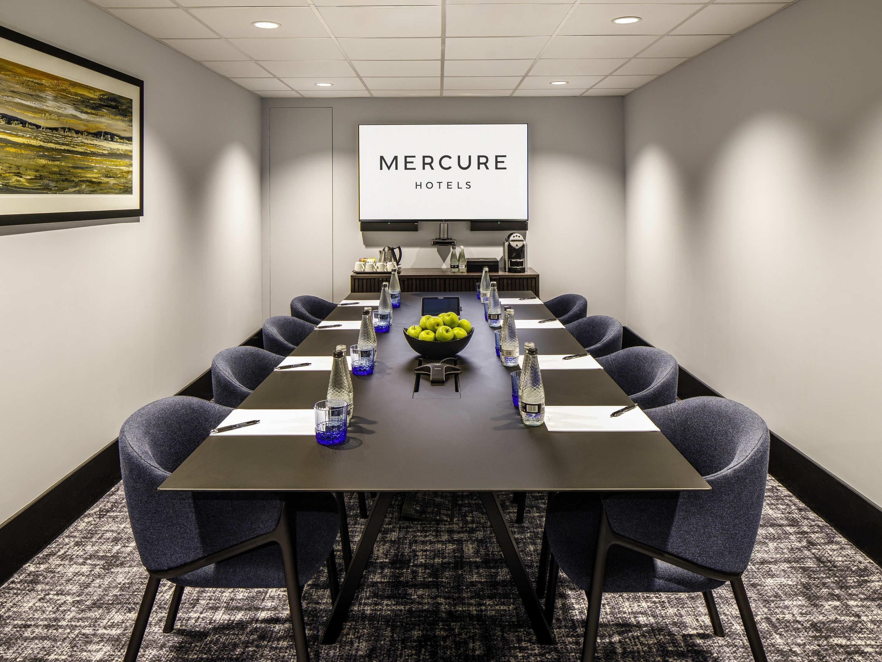 A conference room with a long table, chairs, water bottles, and a fruit bowl.