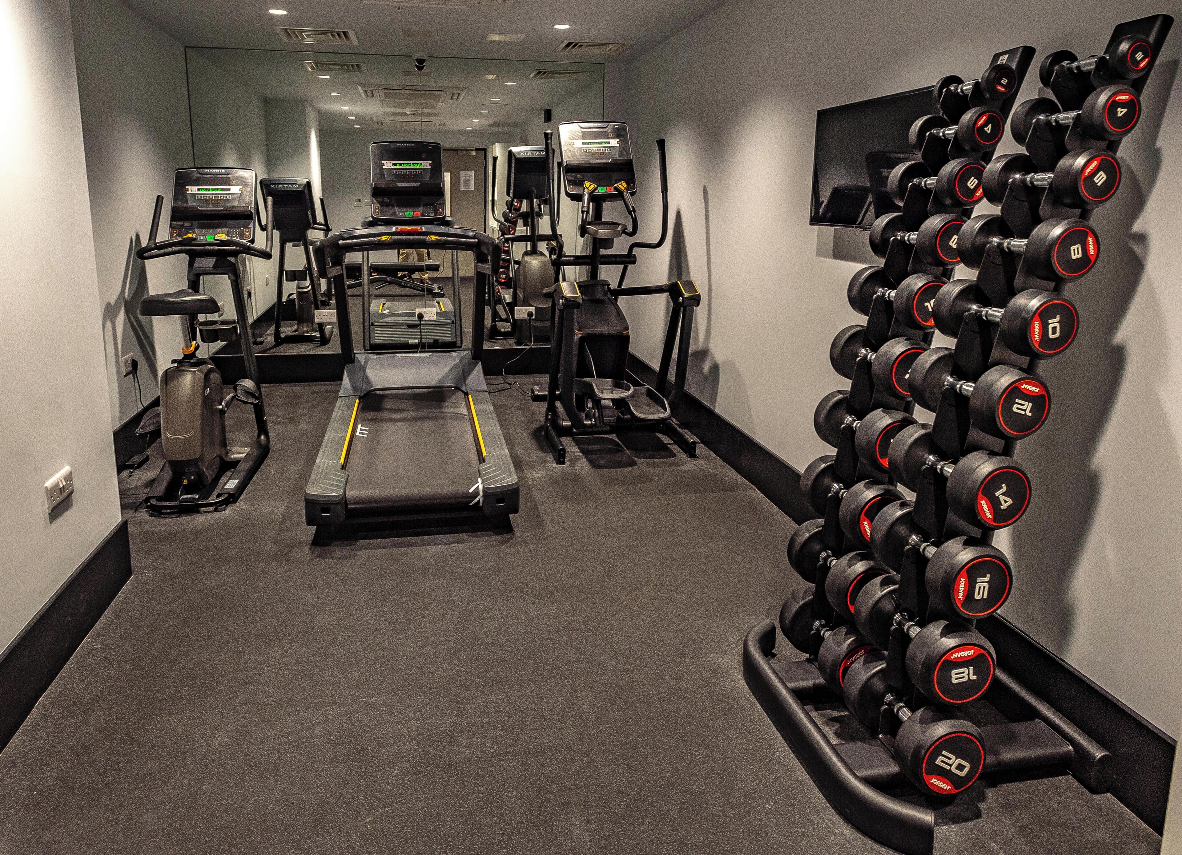 A gym with treadmills, elliptical machines, and a rack of dumbbells.