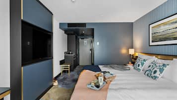 Quarto de hotel com cama, televisão, secretária e casa de banho.