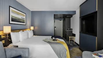 A modern hotel room with a large bed, two bedside tables with lamps, a television, and a small seating area.