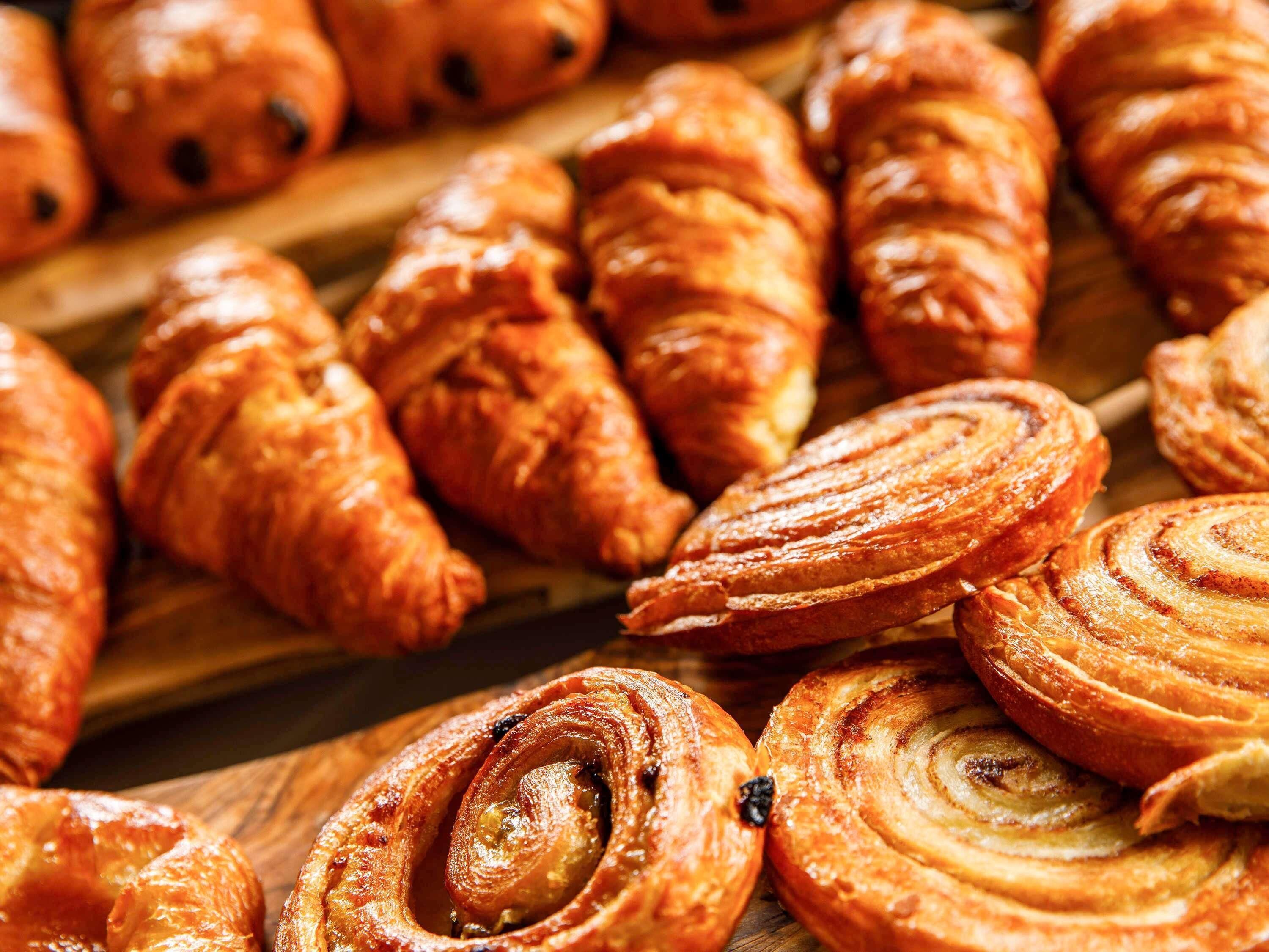 Variedad de pasteles, incluyendo croissants y rollos de canela, sobre una superficie de madera.