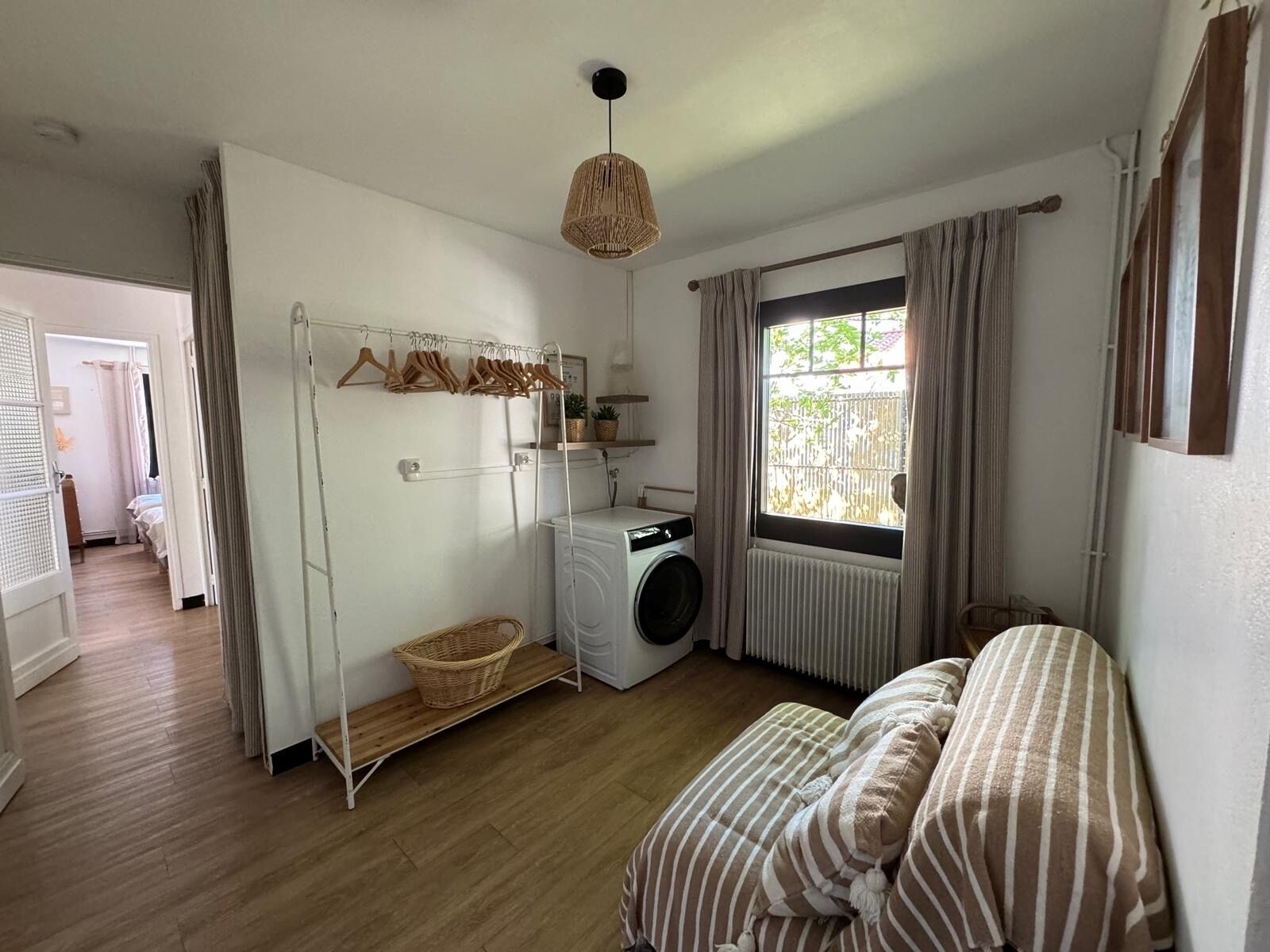 A laundry room with a washing machine, drying rack, and a window with curtains.