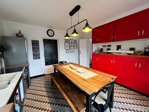 A kitchen with a wooden table, red cabinets, a blackboard with writing, and a clock on the wall.