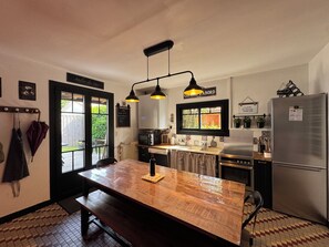 A kitchen with a wooden table, pendant lights, a refrigerator, and a window with a view of greenery. - House in Arcachon, 900 meters from the beach. (Andernos-les-Bains)