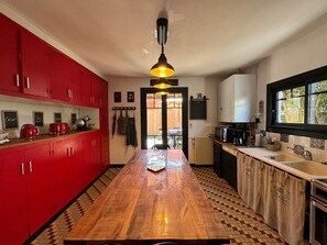 A kitchen with red cabinets, a wooden table, and a hanging light fixture.