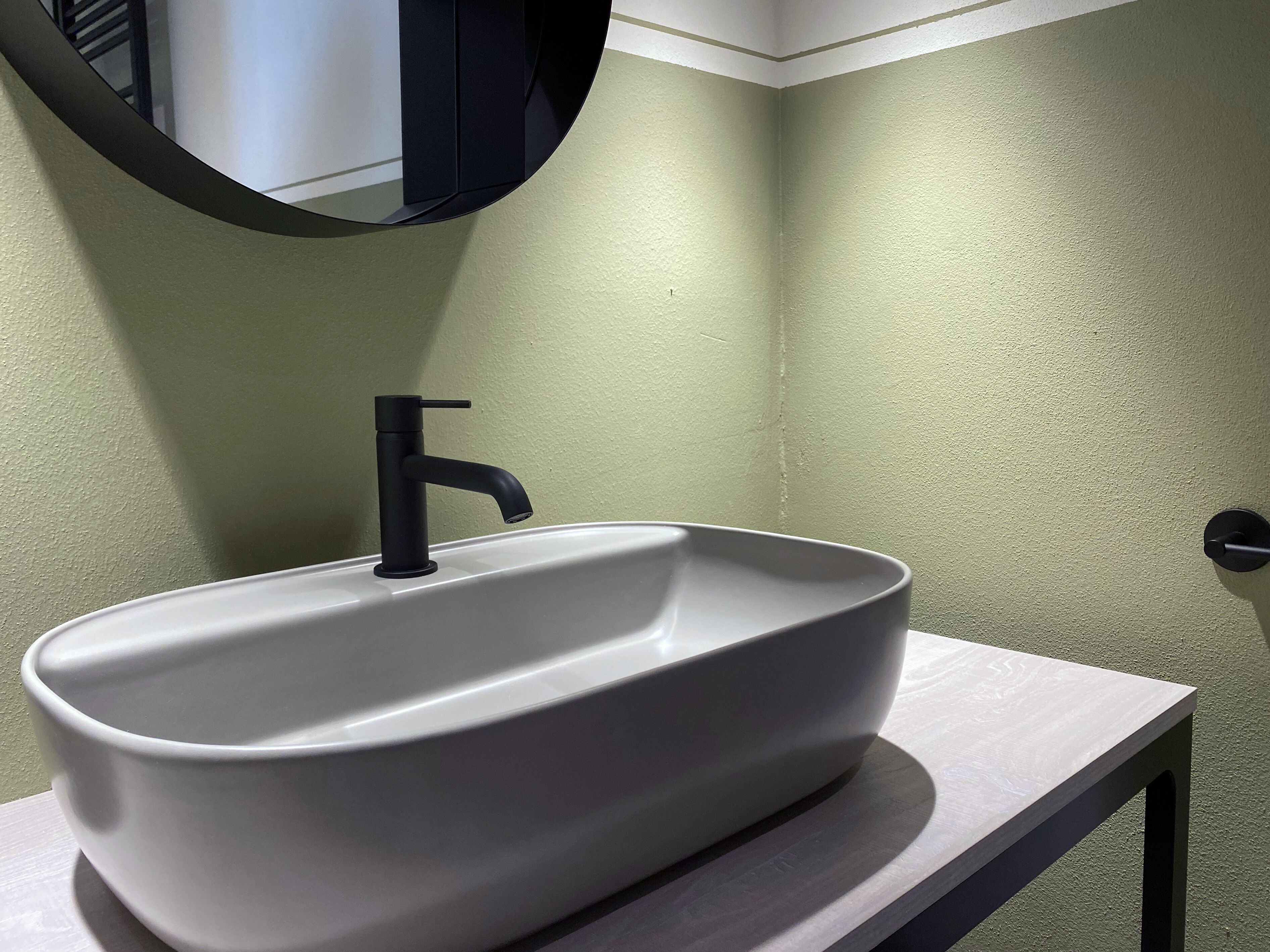 A bathroom with a white sink, black faucet, and a round mirror on a white countertop.