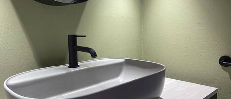 A bathroom with a white sink, black faucet, and a round mirror on a white countertop.