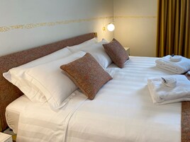 Una cama bien tendida con sábanas blancas, dos almohadas decorativas y un juego de toallas dobladas.