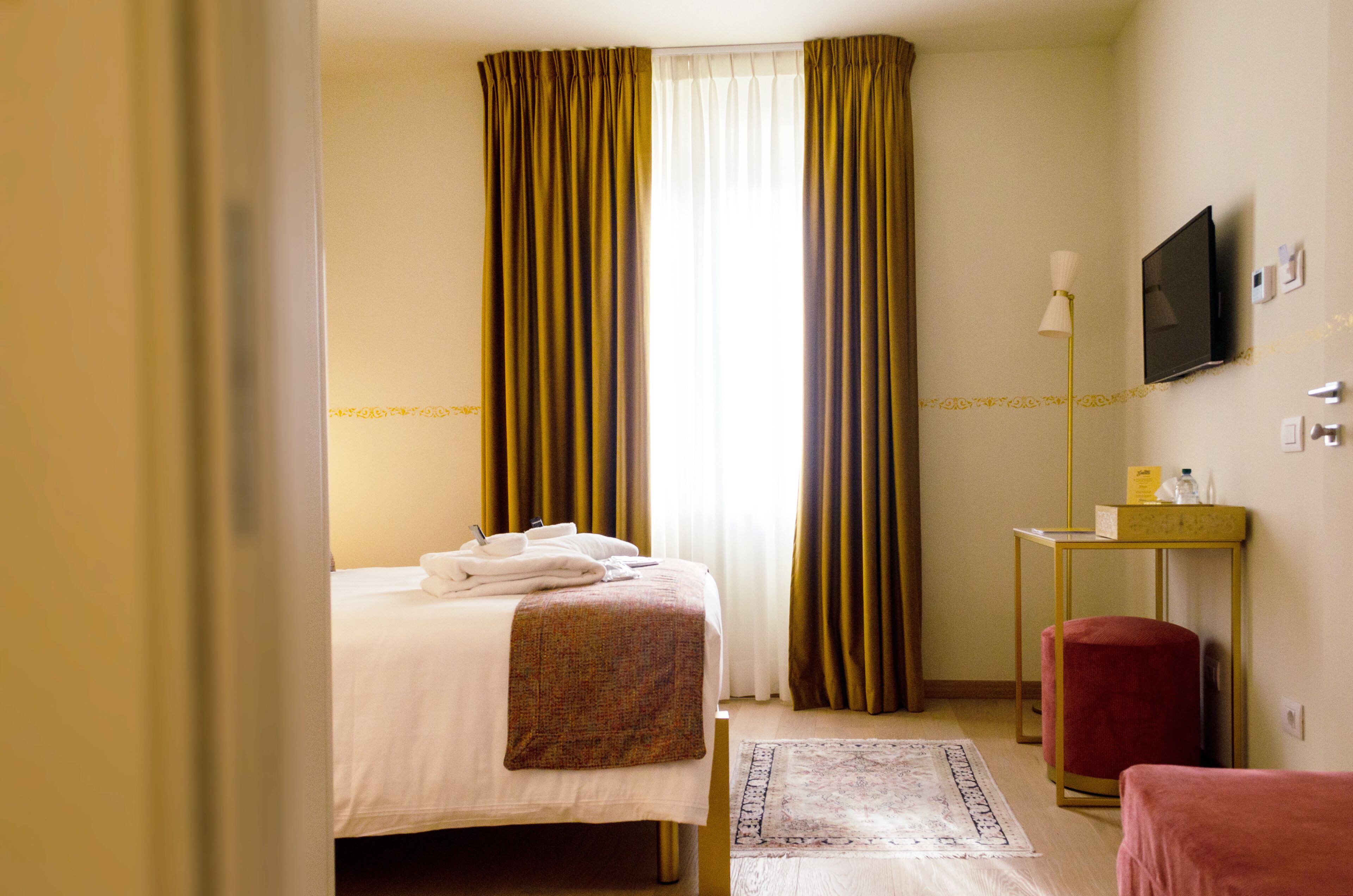 Una camera d'albergo con un letto, una scrivania, una televisione e una poltrona rossa.