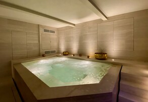 Un jacuzzi grande y rectangular con superficie de agua cristalina, rodeado de paredes color beige y un techo con vigas a la vista.