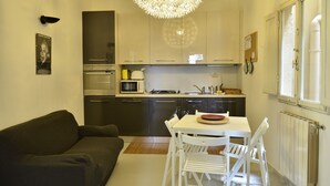 A compact kitchen with modern appliances, a dining area with white chairs, and a large chandelier. - Pitti Three - Two Bedroom Apartment, Sleeps 4 (Firenze)