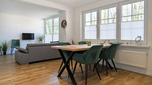 Un comedor moderno con una mesa de madera, sillas tapizadas en verde, un sofá gris y un televisor de pantalla plana montado en la pared.