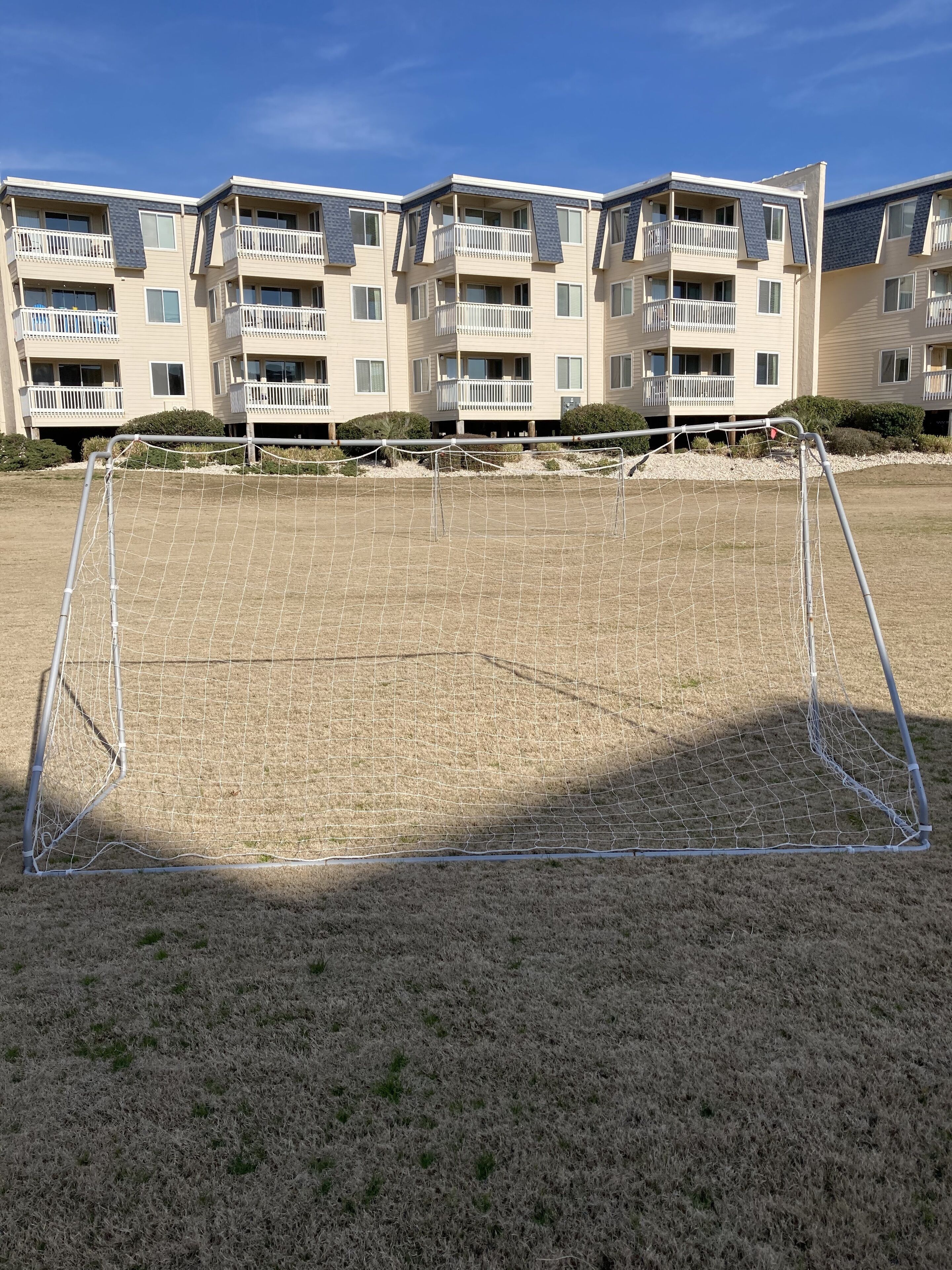 A soccer goal in a grassy field with a multi-story building in the background.