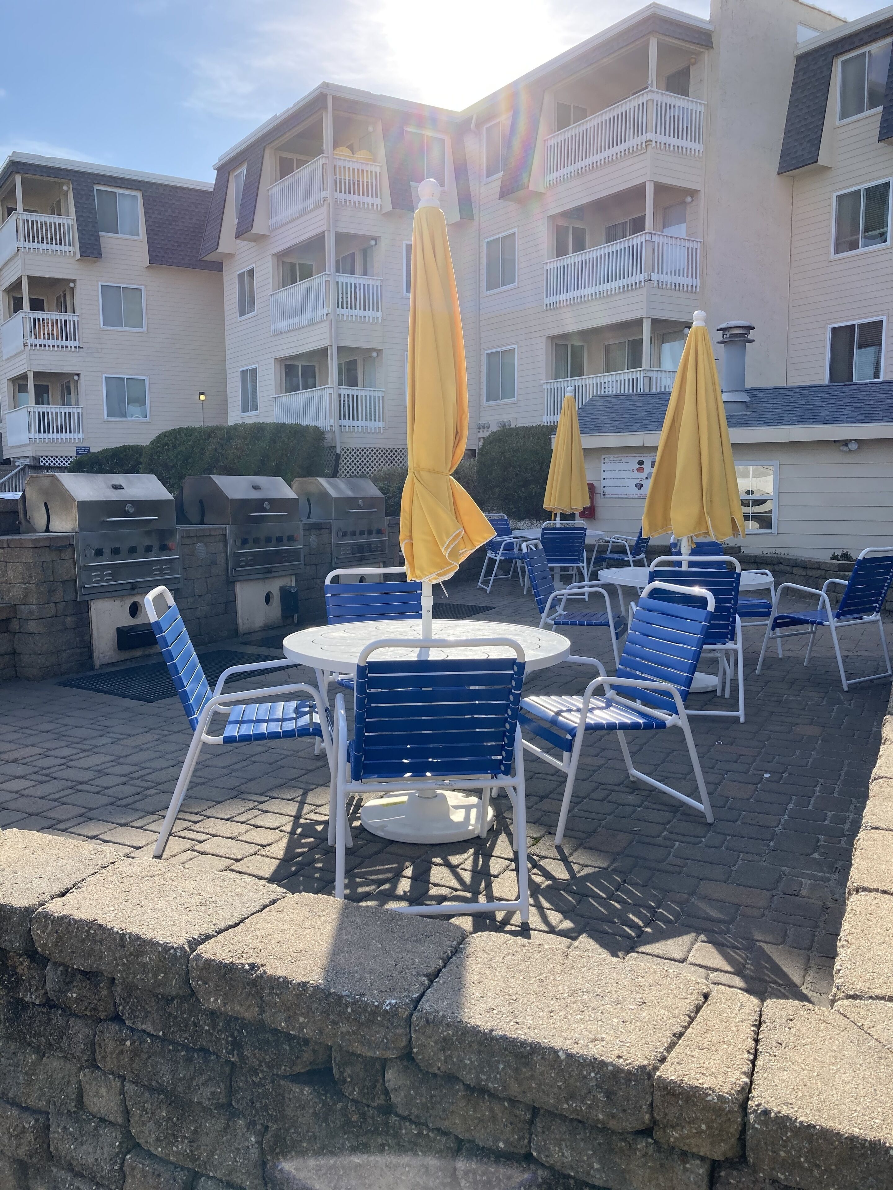 A patio area with outdoor seating, a barbecue grill, and a building with balconies in the background.