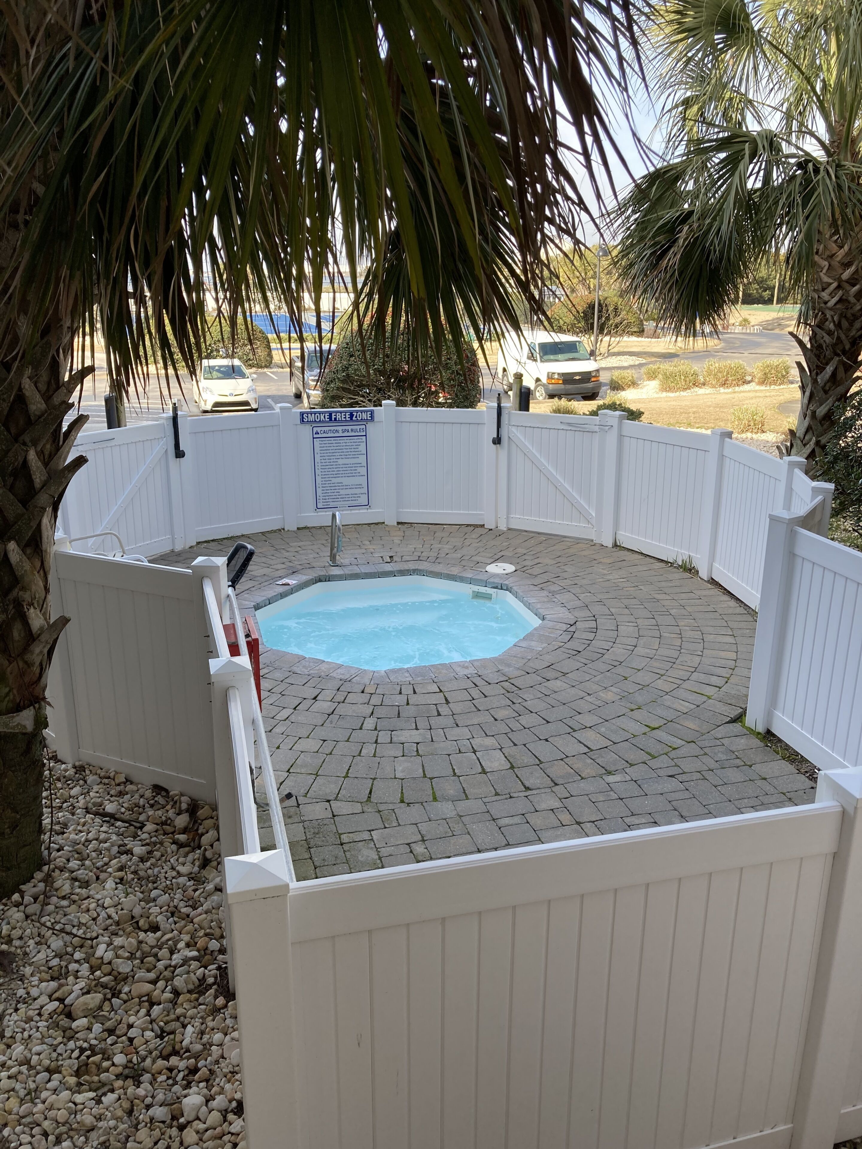 A backyard with a swimming pool surrounded by a white fence, a 'SMOKE FREE ZONE' sign, and a palm tree.