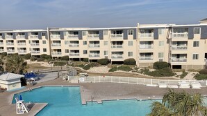 Un espace piscine doté d’une terrasse en bois, d’un poste de surveillance pour le sauveteur et d’une clôture blanche qui entoure la piscine.