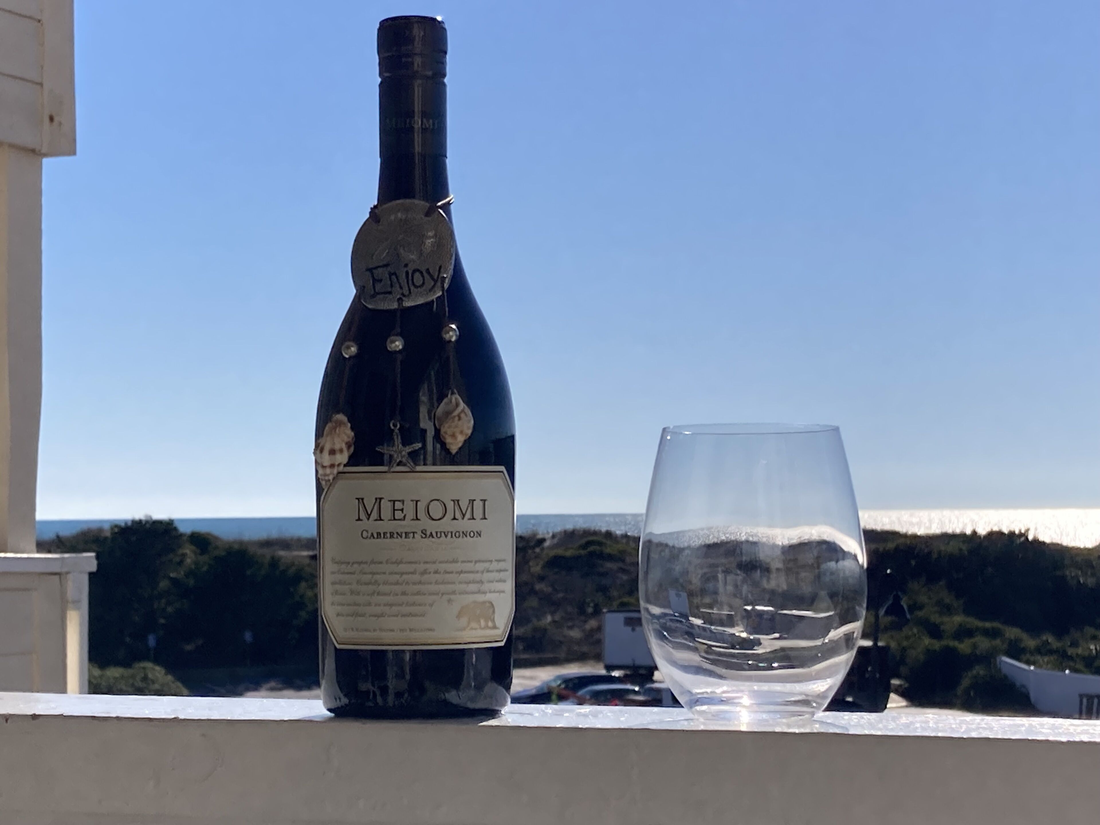 Eine Flasche Meomi Cabernet Sauvignon und ein leeres Glas auf einem Balkon mit Blick auf das Meer.
